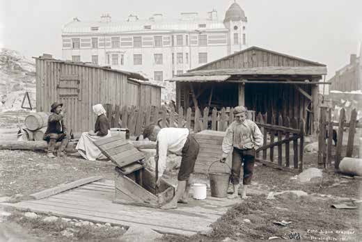 Kallion Linjoilla asuttiin vielä 1911 vaatimattomastikin. Pojat nostavat vettä Viides linja 5:n kaivosta, mutta taustalla Kaikukuja 5:n uudessa kivitalossa nykyajan mukavuuksia on jo käytössä.