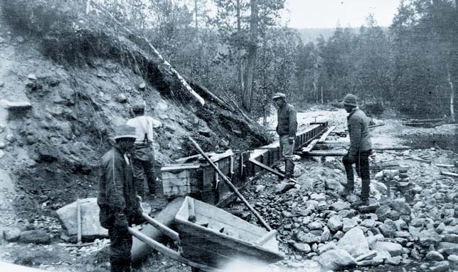 Kullankaivajia Inarin Palsinojalla vuonna 1923. Kuva-alan eteen on tehty pato ja maa-ainesta lapioidaan ränniin. Kuva R. Rehn, Museoviraston kuva-arkisto.