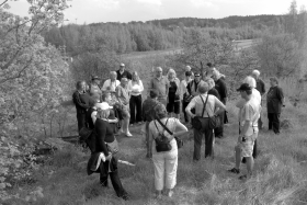 Retkeläiset kerääntyneinä rehevän kasvuston ympäröimään kallionotkelmaan. Taustalla näkyy Hirvensaon Puistotietä.