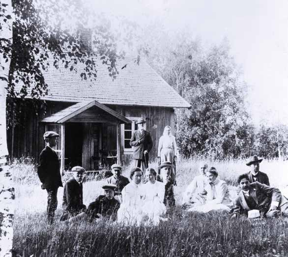Syvälahden torppa eli Aleksis Kiven kuolinmökki 1910-luvun alussa. Etualalla Krapin tilan isäntäväki Maiju (3. oikealta) ja Klas Holma vieraineen pihamaalla.