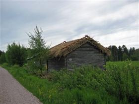 Olkikattoisen ladon katto näyttää viime aikoina uudistetulta. Metsänpuoleisen ladon katto on peltiä. Ladot kuuluvat Isolan talolle.