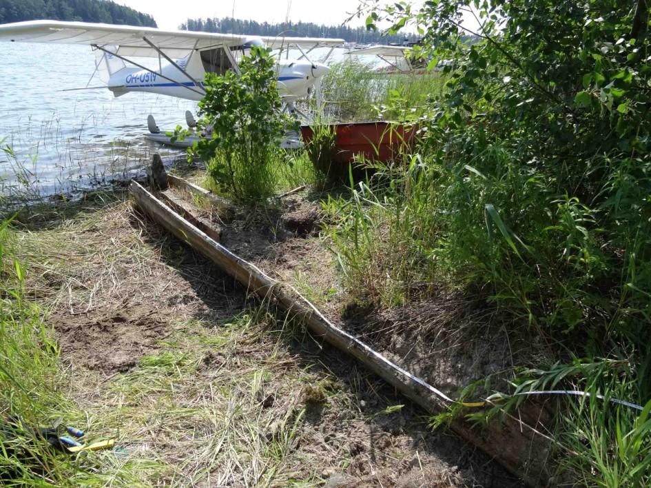 kohteesta saataisiin parempia kuvia. Kyljen ulkopuolella maan sisältä törröttävän puuosan selvittämiseksi tehtiin koekuoppa (kuva 12), joka kaivettiin kenttälapiolla ja lastalla.