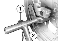 Löystytä etupyörän huoltopukin säätöruuvit 1. Työnnä molempia kiinnitystappeja 2 niin pitkälle ulospäin, kunnes etuhaarukka sopii niiden väliin.