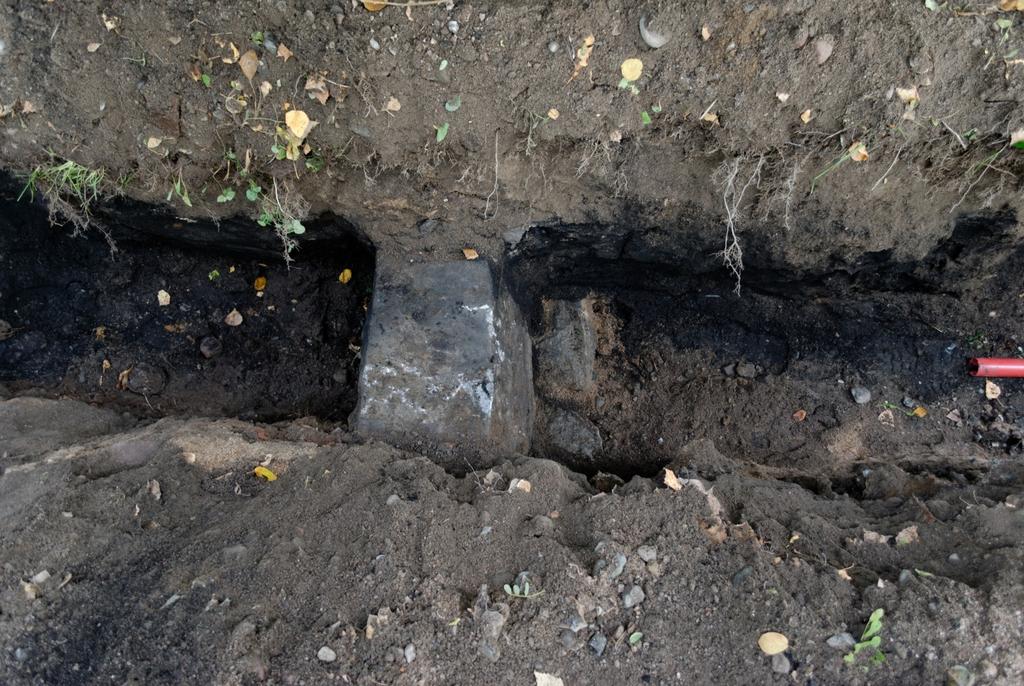 Kuva 7. Kaivannosta 5 löytynyt pohjoisempi rakennuksen perustuskivi ja sen sisäpuolen anturaa lännestä. Kaapeliputken halkaisija 5 cm.