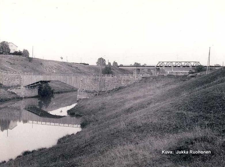 12 Kuva 7. Vuonna 1967 otetussa valokuvassa näkyy sillan tukiansaita peittänyt lautaverhous. Taustan rautatiesillan takaa häämöttää ykköstien 1950- luvulla rakennettu silta. (Kuva: Jukka Ruohonen.