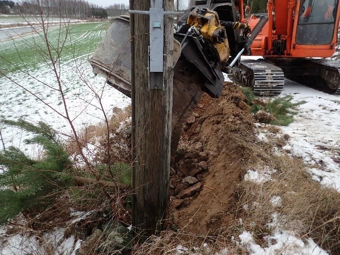 Kaivinkone kaivoi pylvään jalkojen itä- ja länsipuolelta noin 50 cm kerroksen maata, minkä jälkeen kaivinkoneen koura pystyi nostamaan pylväät pois maasta. Vasen: sähköpylväs B ennen sen poistamista.