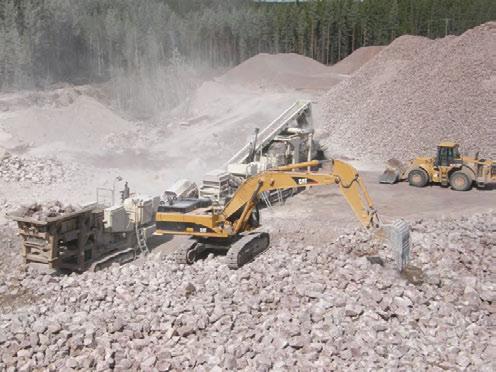 Kuva 3.8. Kolmevaiheinen kivenmurskauslaitos, etualalla laitosta syöttävä kaivinkone, oikealla mursketta siirtävä etukuormaaja. Taustalla murskeen varastokasoja.