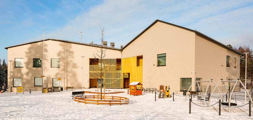 RAKENNETTU PROJECTS TOUKOVUOREN PÄIVÄKOTI Kaksoisharjakattoinen rakennus rajaa leikkipihaa kadusta. Lasten sisäänkäynnit ovat suojaisassa syvennyksessä keltaisen rimoituksen takana.