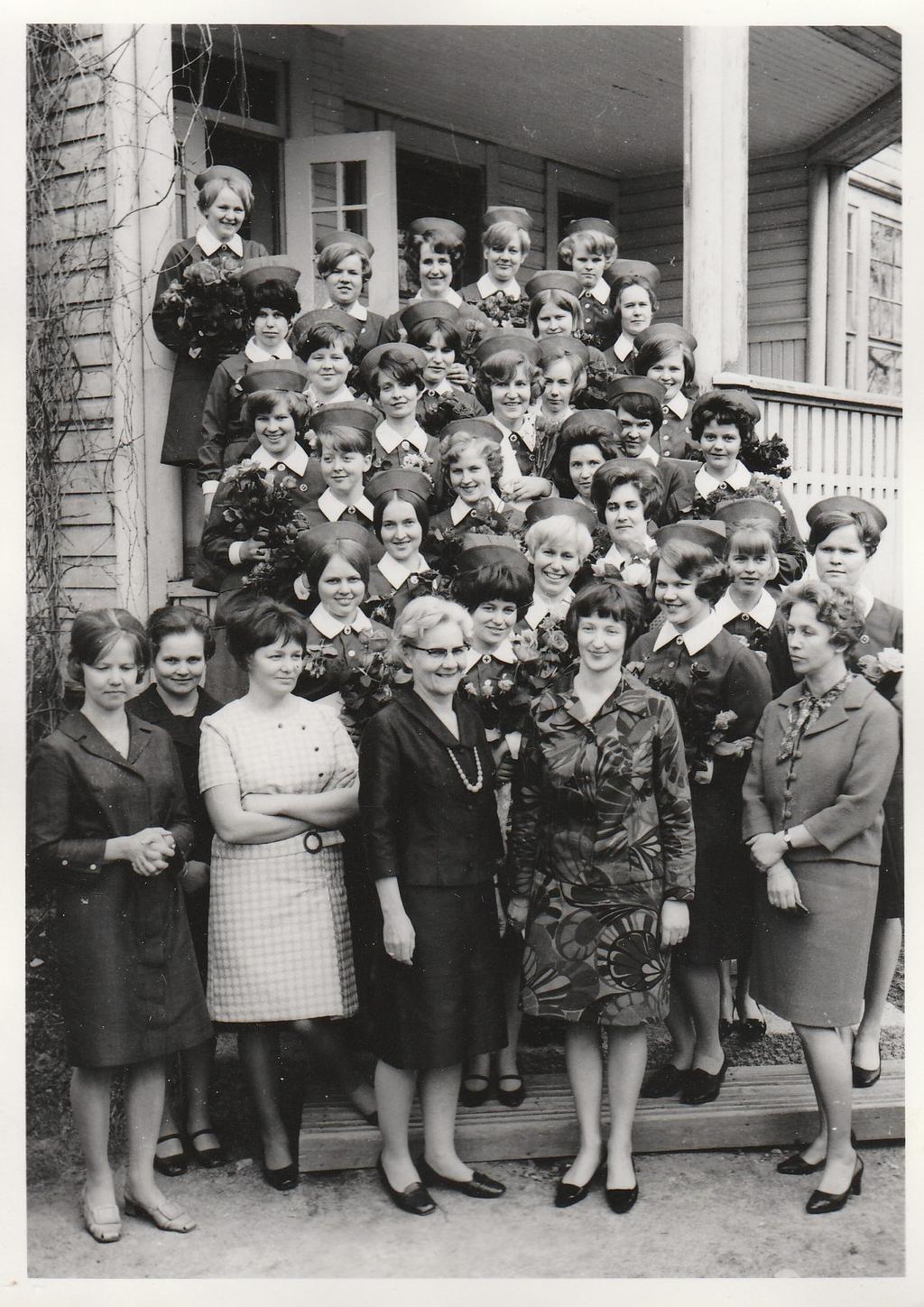 Keväällä 1969 valmistuneet kodinhoitajat ryhmäkuvassa opiston portailla. Eturivissä opettajia, oikealla apulaisjohtaja, talousopettaja Maija-Leena Akiala.