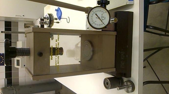 KUVAT 6 ja 7. Vasemmalla tabletin valmistukseen käytetty sylinteri ja laitteisto. Oikealla pommikammion kansi ja näytetabletti upokkaassa (kuva Tarja Seppänen).