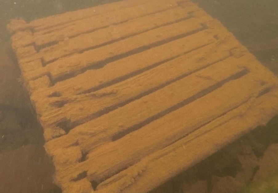 Arkku on kaatunut pystyasennosta kohti syvempää vettä ja täytekivet ovat vyöryneet osittain ulos arkusta. Arkkua kuvattiin sukelluksen yhteydessä videokameralla.