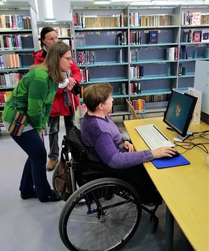 Tuija-Kaisa Teikari opasti Raija Kortelaista asiakastietokoneen käytössä. Pyörätuoli mahtui sopivasti pöydän alle. Pirjo Hoikkanen seurasi sivusta.