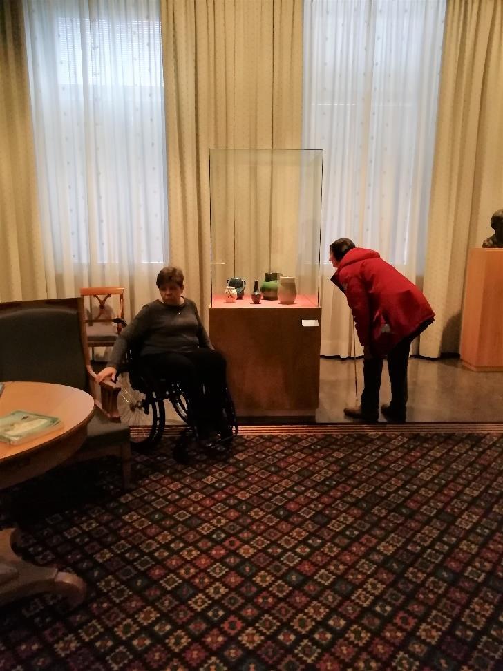 Pirjo Hoikkanen tutki Iirishuoneen keramiikkavitriiniä. Raija Kortelaisen oli vaikea siirtyä vitriinin luo, koska huonekalut ja pehmeä matto loivat esteitä reitille.
