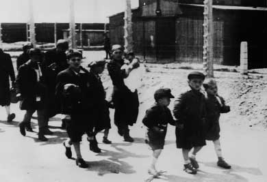 Naisia ja lapsia, jotka ovat aloittaneet 1,5 kilometrin vaelluksen kohti Krematorio 4:ä tai 5:ttä Auschwitz- Birkenaussa. Taustalla näkyy joitakin tavaravaunuja laiturin vierellä.