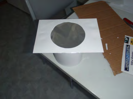 Vaihe 8 Liimaa toinen reiällinen kartonginpala suodinkalvon päälle kuvan 8 osoittamalla tavalla. Teippaa reunat kiinni. Kun reunat on teipattu ja liima kuivunut, on aurinkosuodin valmis käyttöön!