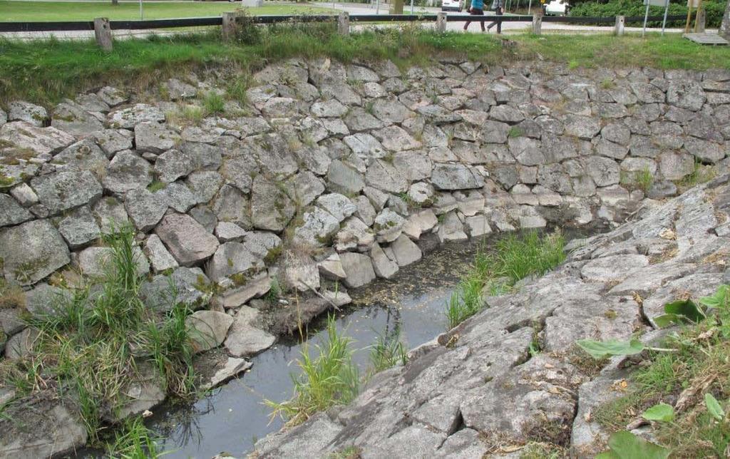 Keskivaiheen pohjoispuolella on muurista kivi poissa ja aukon ympärillä olevat kivet ovat kääntyneet sijoiltaan. Kuva 17. Osa alimmasta kivikerrasta on nurjahtanut osittain pois arinahirren päältä.