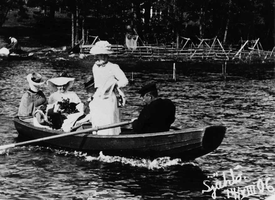 Sama seurue jatkaa matkaansa soutuveneellä. Airoissa Armas Holländer ja seisaaltaan tähystämässä Aina Olsoni.