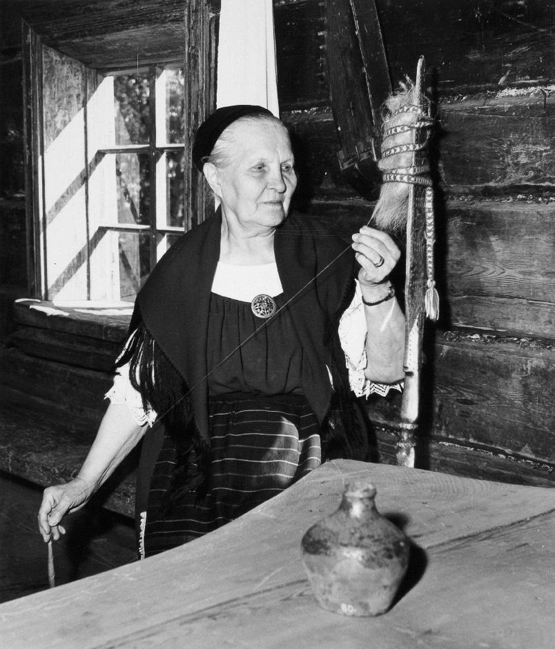 237 Elmi Tšokkinen kehrää värttinällä Seurasaaren ulkomuseon Pertinot šan karjalaistalossa vuonna 1958. István Rácz. Museoviraston Kuva-arkisto S. 28:79.