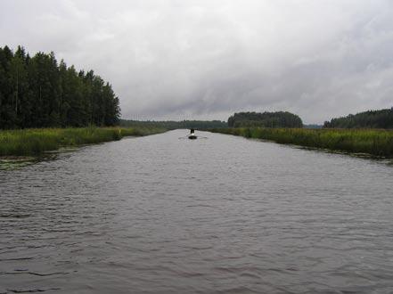 Kuva 12. Lassilanjoki virtaa Inhottujärven itäpäässä pitkän matkan penkkojen reunustamassa uomassa. Lassilanjoen rantapenkkaan tehtävät virtausaukot ovat tulleet esiin myös mm.