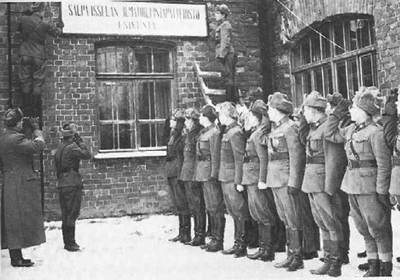 Oikeanpuolessa kuvassa SALPITPSTO on juuri saanut nimensä ja patteriston henkilöstö kunnioittaa esikunnan seinälle asetettua uutta nimikylttiä 1.1.1957.