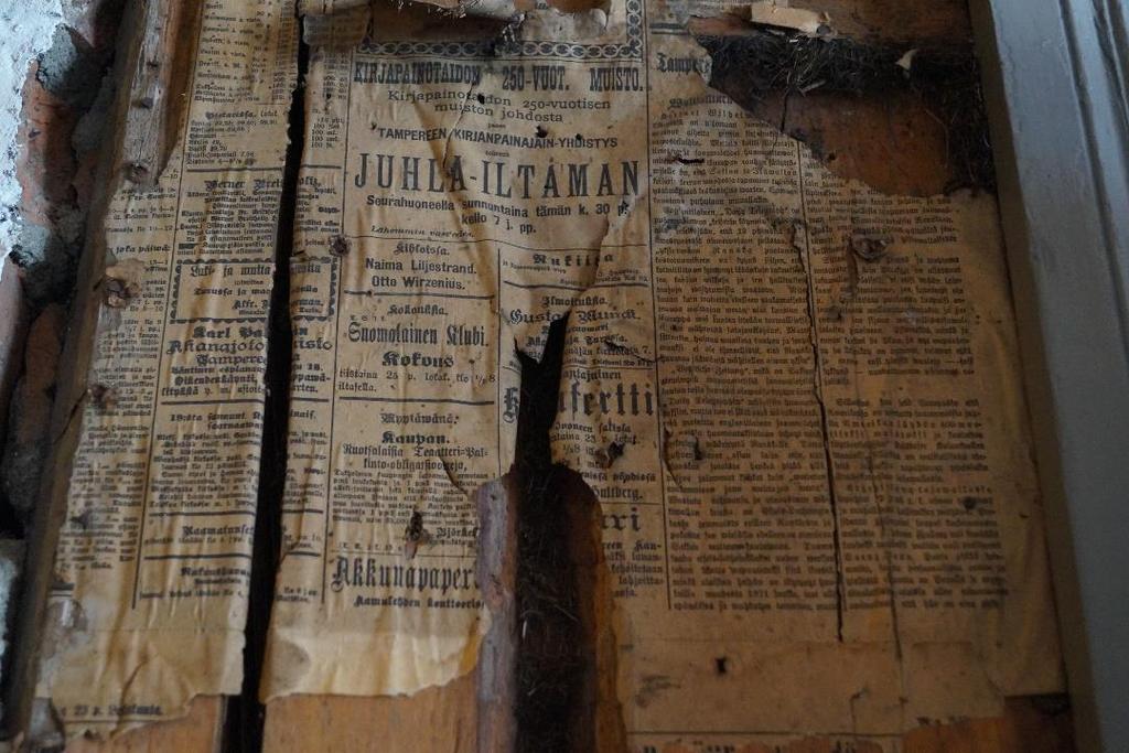 Seinään liisteröity sanomalehti (Vattulainen 2017) Paperin päällä katonrajassa on jäljellä tapettifragmentteja.