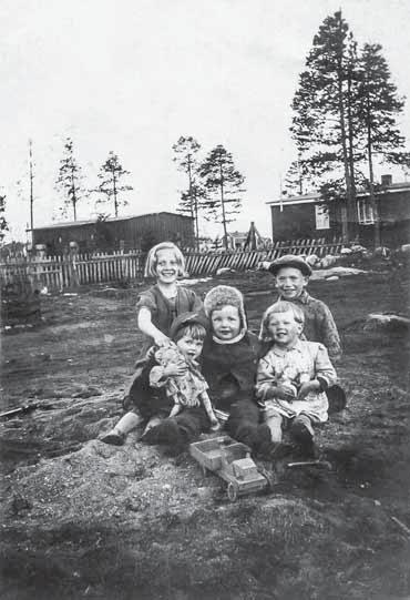 Harvinainen kuva, jossa näkyy OT:n leirialueen parakkeja lasten takana. Kuva: Sirkka Lampelan valokuva-albumi. danaikaisia esineitä, mm. konekiväärivyö, näkyville. 479 Sirkka Lampelan os.