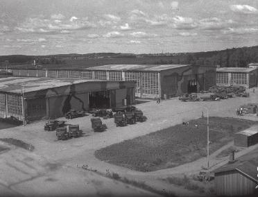 Kuva: Kantatehdas jatkosodan aikaisessa naamiomaalauksessa. Sakaroita on pidennetty, päädyissä ikkunapintojen tilalla liukuovet. Kuva kaakosta, 1944/1945.